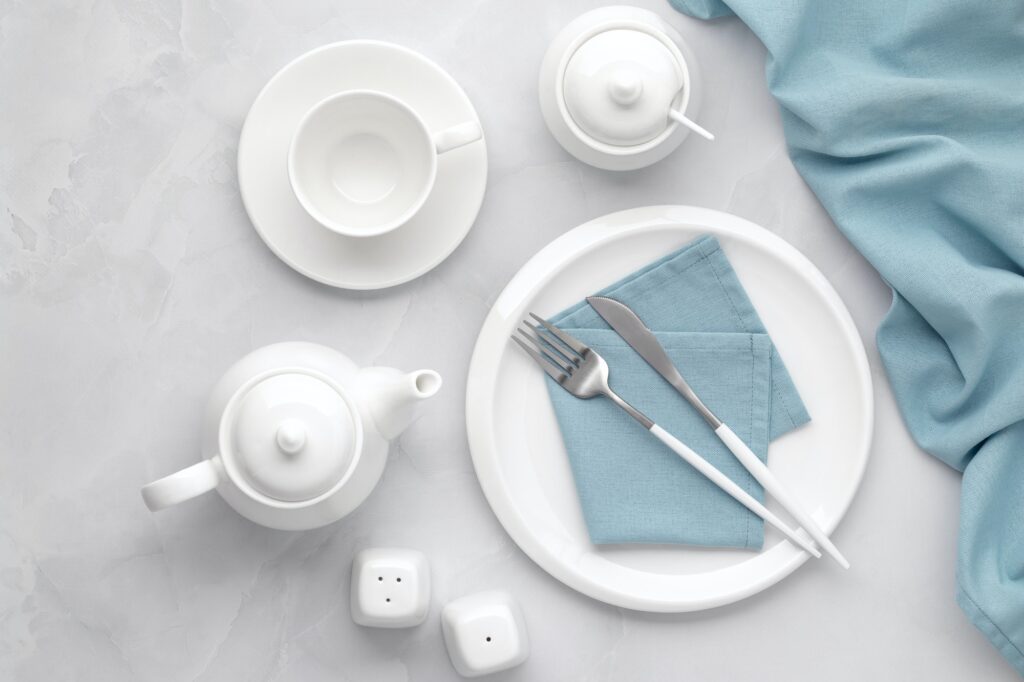 White ceramic tableware and cutlery. Utensils dishware, crockery, teapot and cup on gray marble
